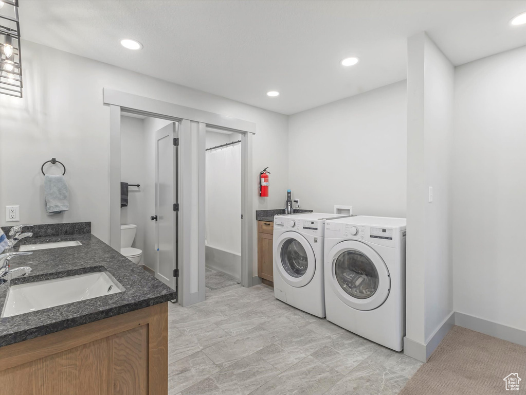Clothes washing area featuring washing machine and clothes dryer, a sink, recessed lighting, and baseboards
