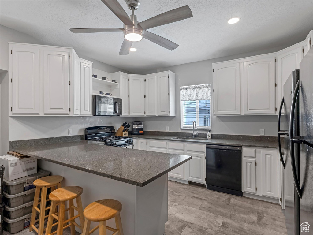 Kitchen with black appliances, a sink, a peninsula, white cabinetry, and recessed lighting