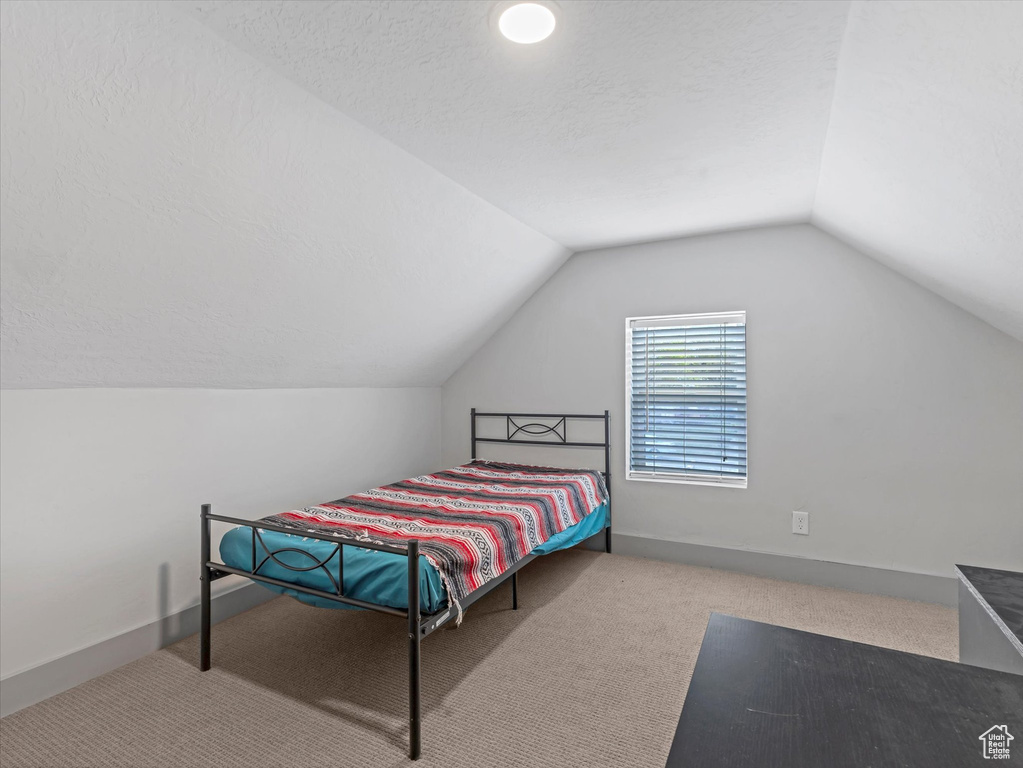 Carpeted bedroom featuring vaulted ceiling, a textured ceiling, and baseboards