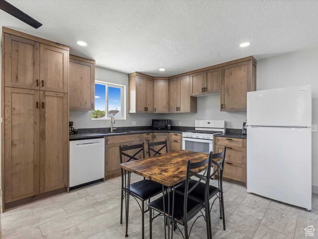 Kitchen featuring white appliances, dark countertops, a sink, recessed lighting, and a textured ceiling