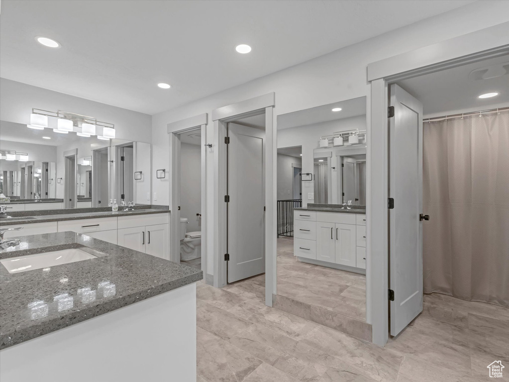 Full bath with toilet, two vanities, and recessed lighting