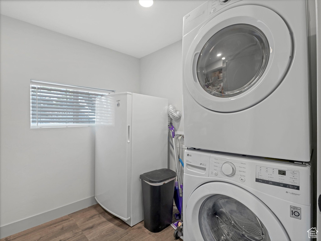 Clothes washing area with stacked washing machine and dryer, wood finished floors, and baseboards
