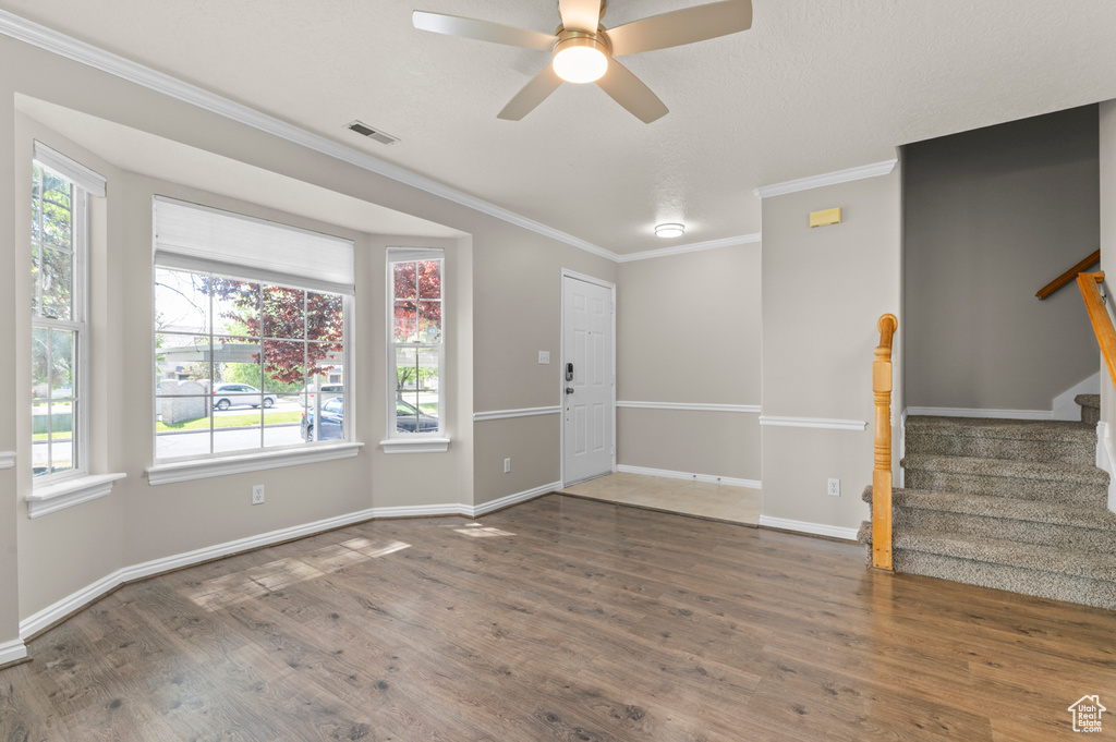 Unfurnished living room with wood finished floors, stairway, ceiling fan, ornamental molding, and healthy amount of natural light