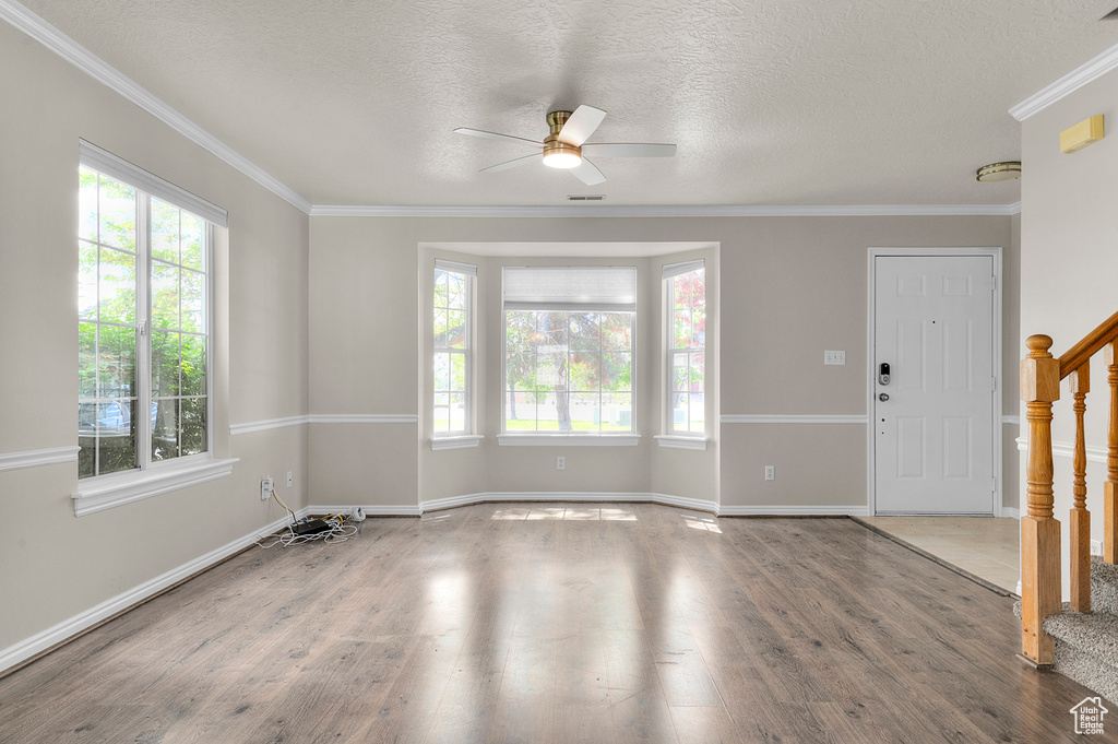 Spare room featuring plenty of natural light, ceiling fan, wood finished floors, ornamental molding, and a textured ceiling