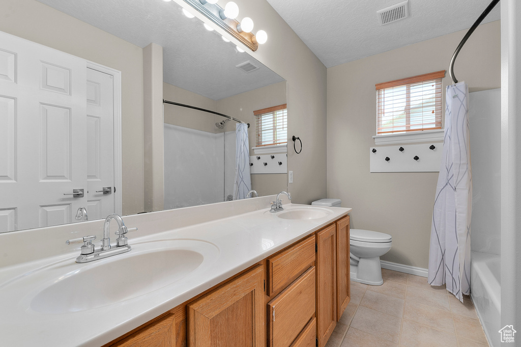Full bathroom featuring toilet, baseboards, double vanity, tile patterned flooring, and shower / bath combo with shower curtain