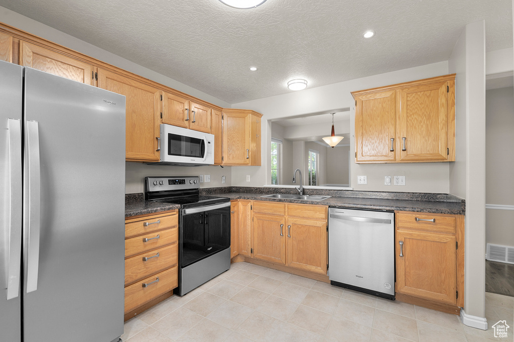 Kitchen featuring appliances with stainless steel finishes, a sink, dark countertops, a textured ceiling, and recessed lighting