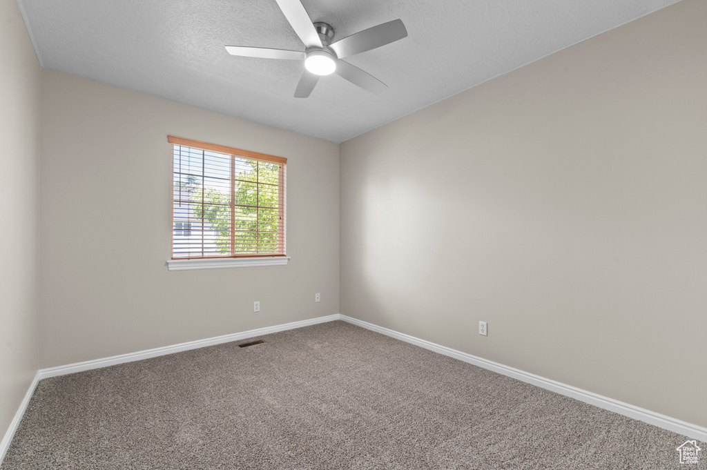 Carpeted empty room featuring a ceiling fan, baseboards, and a textured ceiling