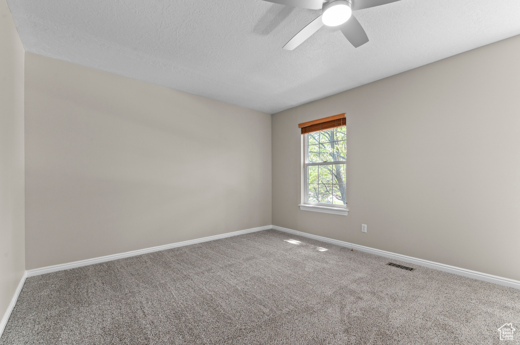 Carpeted spare room featuring baseboards, a textured ceiling, and a ceiling fan