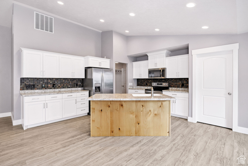 Kitchen featuring stainless steel appliances, tasteful backsplash, a kitchen island with sink, white cabinets, and recessed lighting