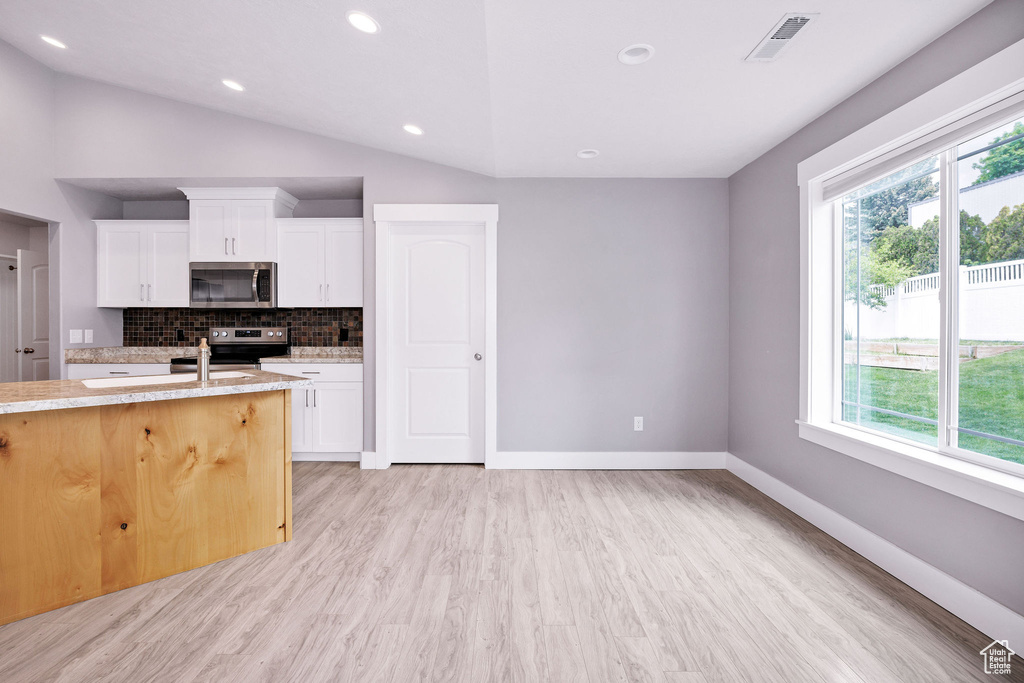 Kitchen with appliances with stainless steel finishes, plenty of natural light, light wood-style floors, decorative backsplash, and vaulted ceiling