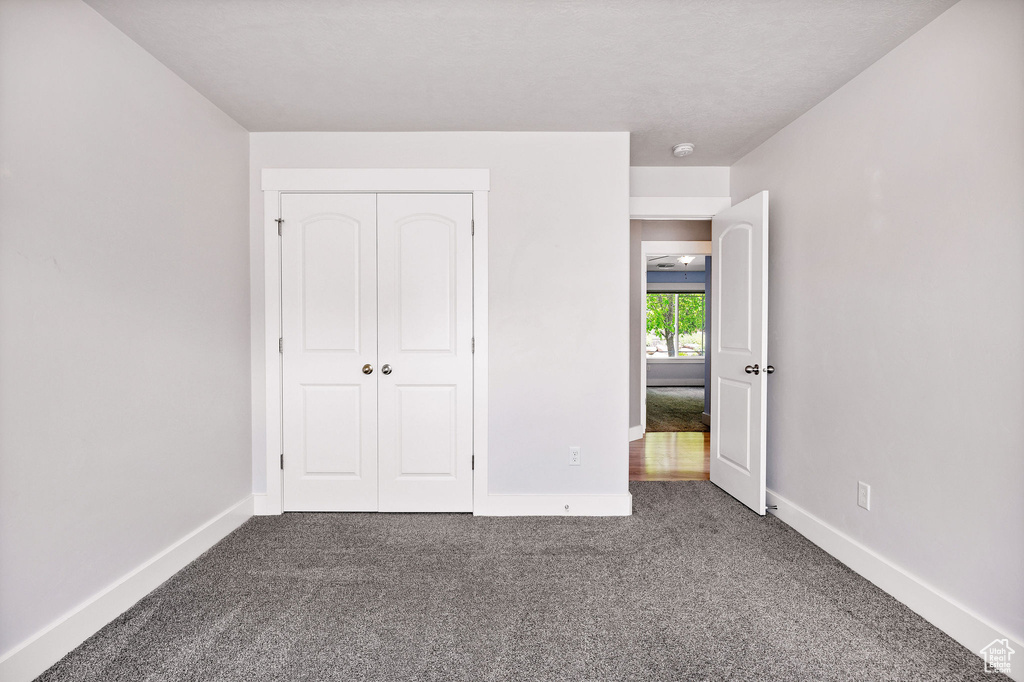 Unfurnished bedroom with dark carpet, baseboards, and a closet