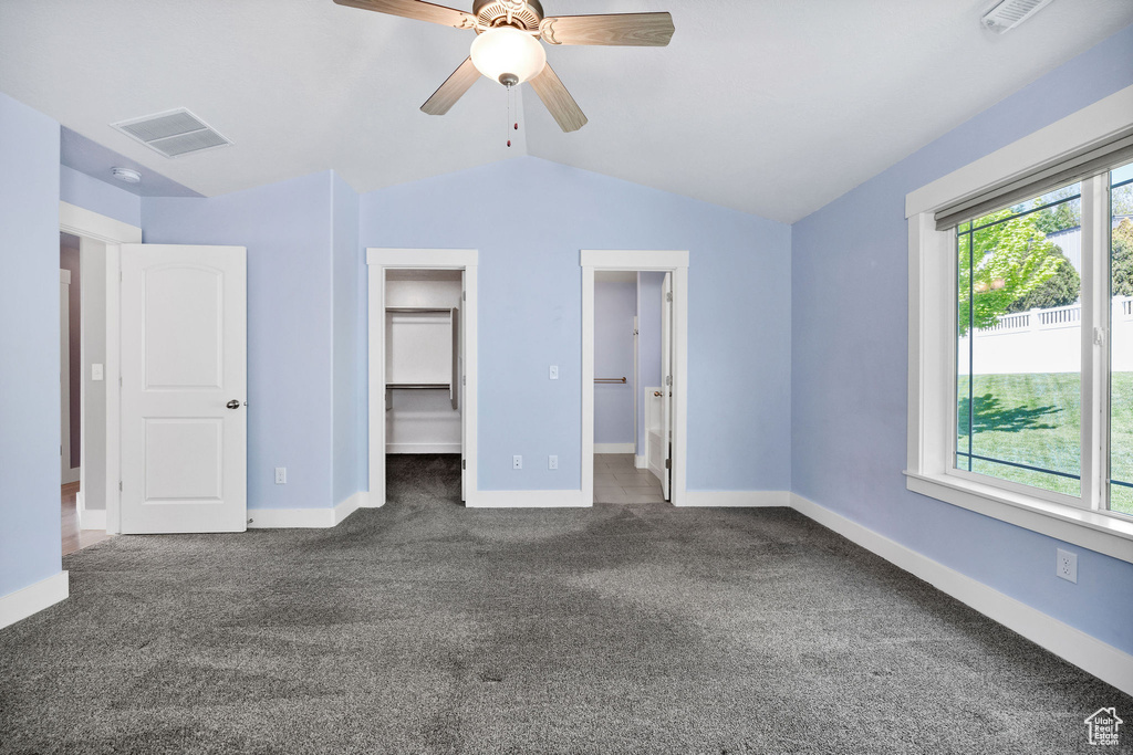 Unfurnished bedroom with carpet, lofted ceiling, a walk in closet, baseboards, and ceiling fan