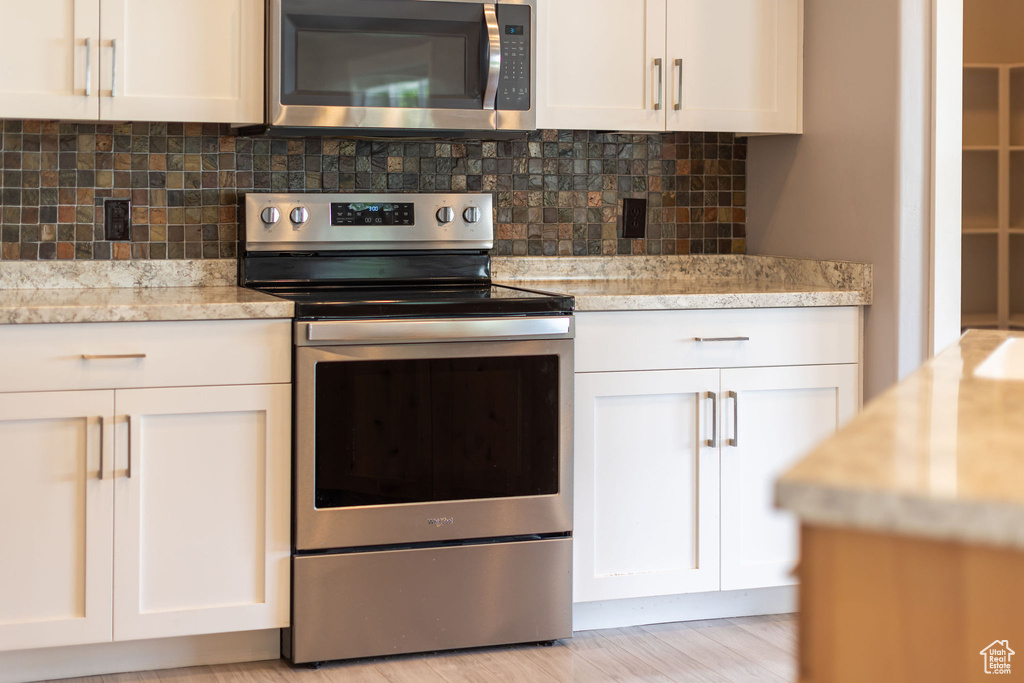 Kitchen featuring appliances with stainless steel finishes, tasteful backsplash, white cabinetry, and light stone countertops