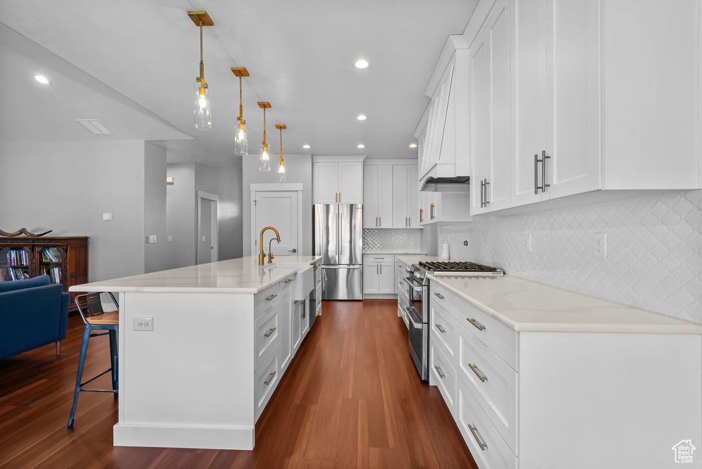 Kitchen with stainless steel appliances, a kitchen breakfast bar, dark wood-type flooring, white cabinets, and recessed lighting