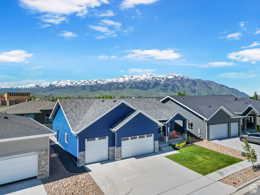 Single story home with stone siding, a mountain view, a garage, driveway, and a shingled roof