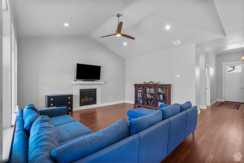Living room featuring wood finished floors, vaulted ceiling, a ceiling fan, a fireplace, and baseboards
