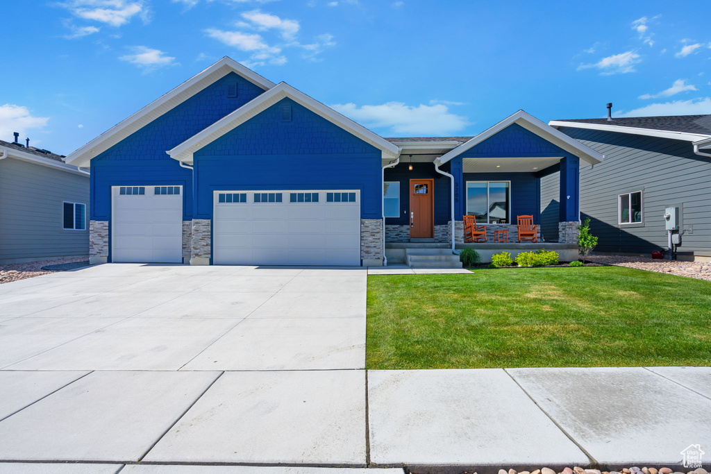 View of front facade featuring covered porch, a garage, a front yard, stone siding, and concrete driveway