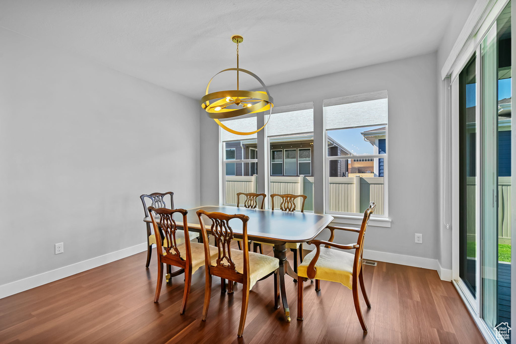 Dining room featuring healthy amount of natural light, wood finished floors, baseboards, and a chandelier