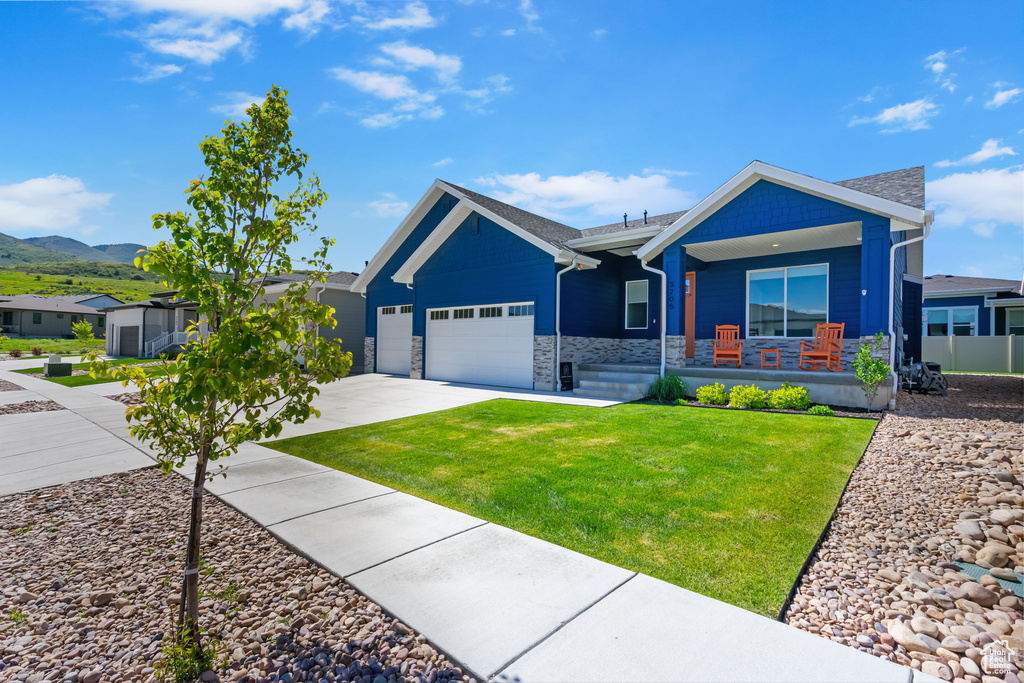 Ranch-style home featuring a porch, a garage, stone siding, a front lawn, and driveway