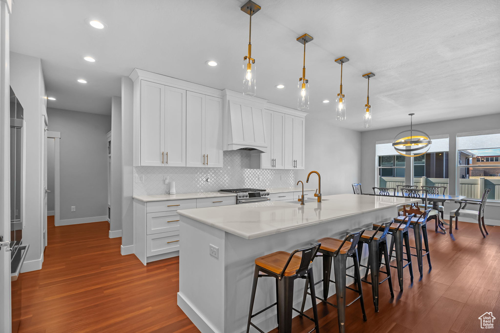 Kitchen with dark wood-style floors, stainless steel gas range, tasteful backsplash, a kitchen breakfast bar, and recessed lighting