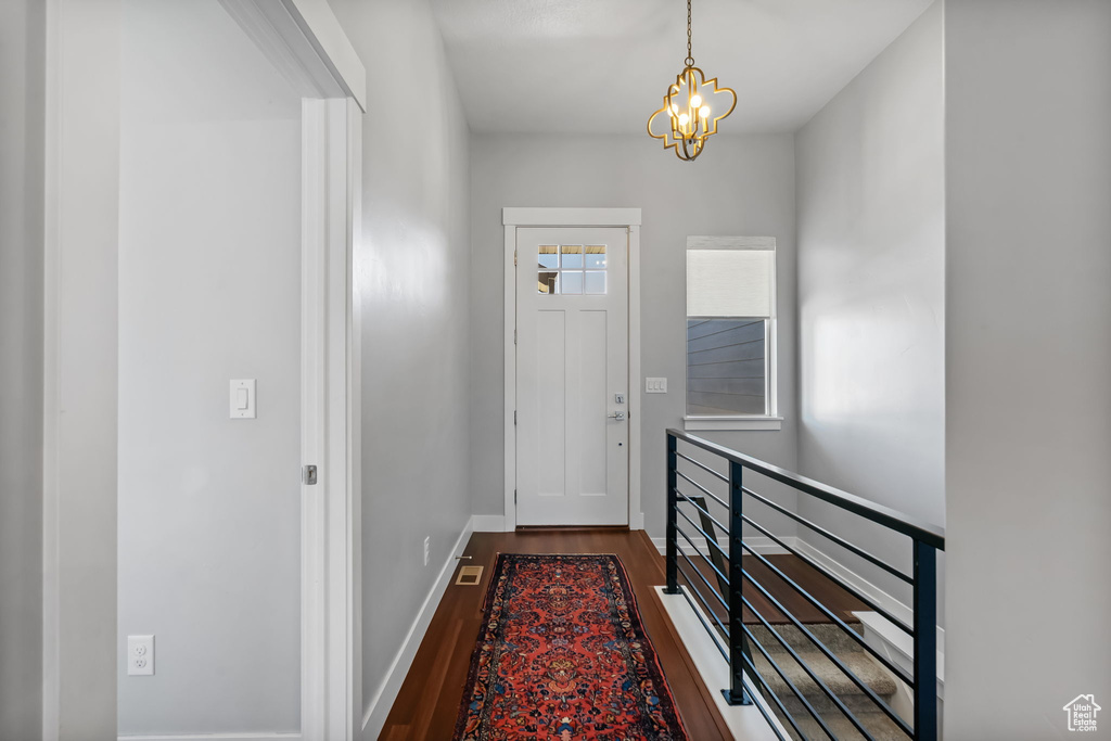 Doorway to outside featuring dark wood-type flooring, a chandelier, and baseboards