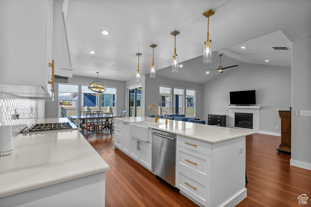 Kitchen featuring dishwasher, dark wood-type flooring, a sink, a fireplace, and lofted ceiling