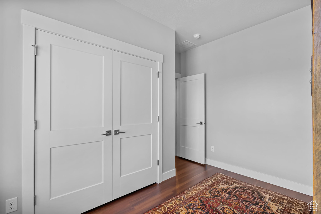 Unfurnished bedroom featuring dark wood-style flooring, a closet, and baseboards