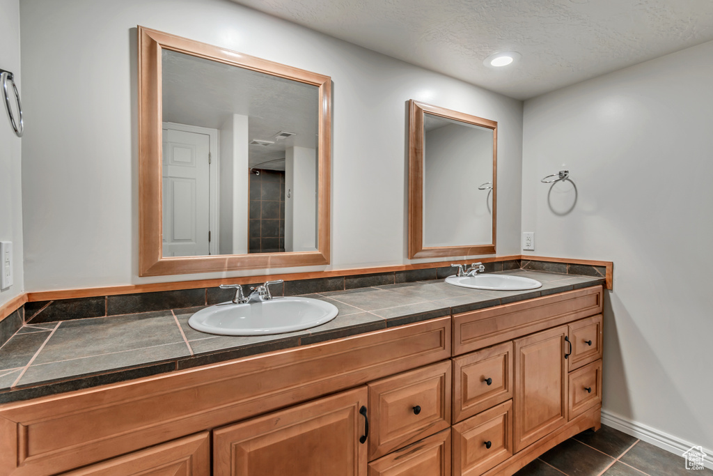 Full bathroom featuring double vanity, baseboards, tile patterned floors, and a textured ceiling