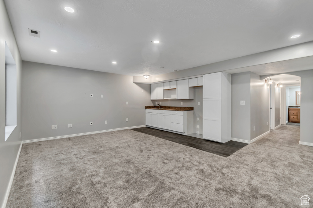 Unfurnished living room featuring carpet flooring, baseboards, arched walkways, recessed lighting, and wet bar