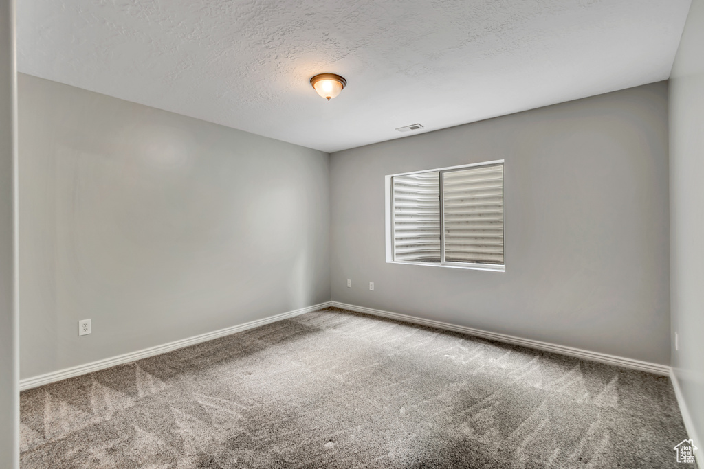 Carpeted empty room featuring baseboards and a textured ceiling