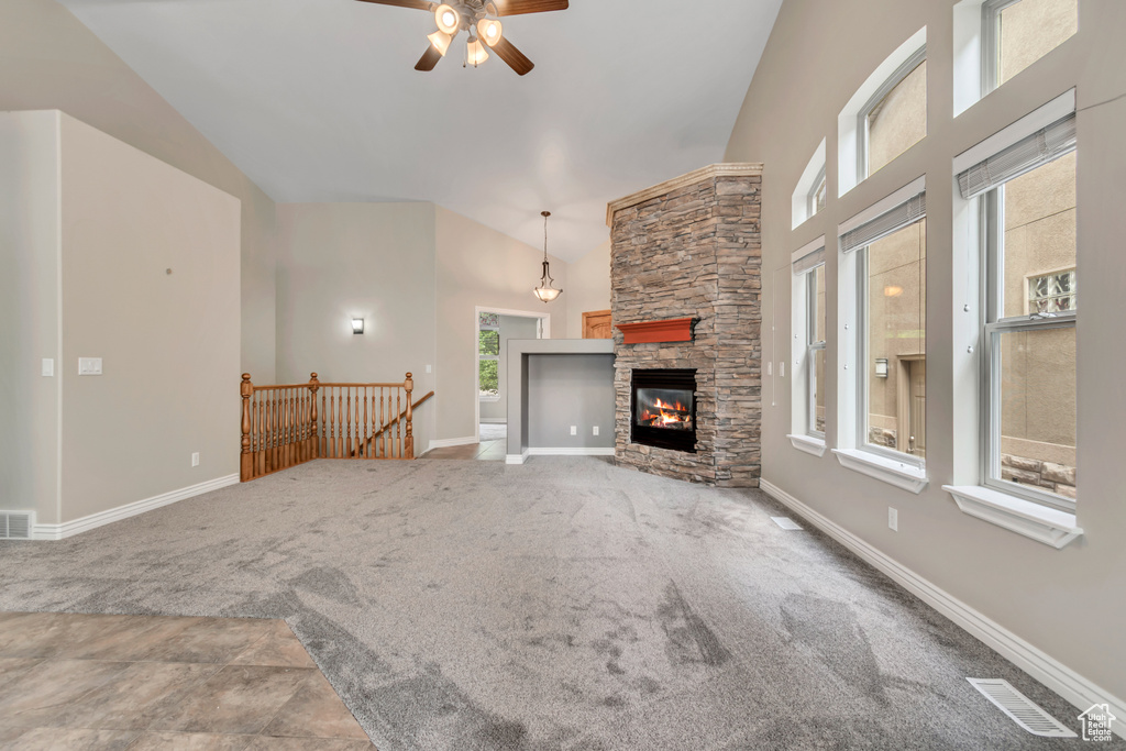 Unfurnished living room with a ceiling fan, high vaulted ceiling, carpet floors, baseboards, and a stone fireplace