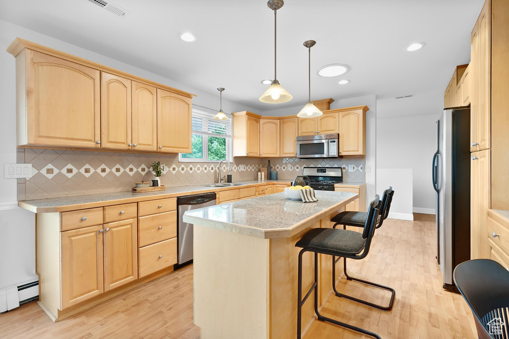 Kitchen with stainless steel appliances, light brown cabinetry, a sink, a breakfast bar area, and light wood-type flooring