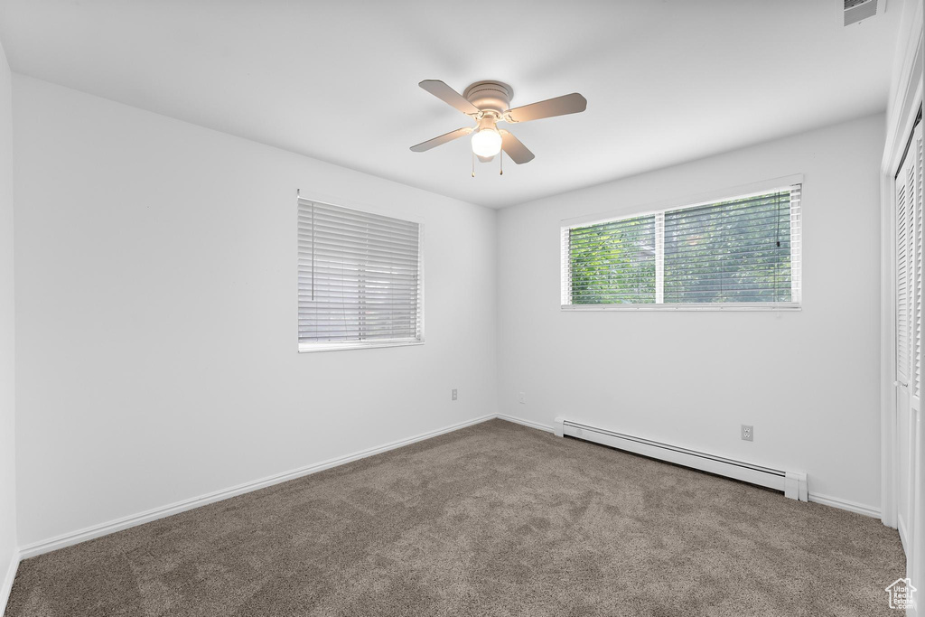 Empty room with baseboard heating, ceiling fan, carpet floors, and baseboards
