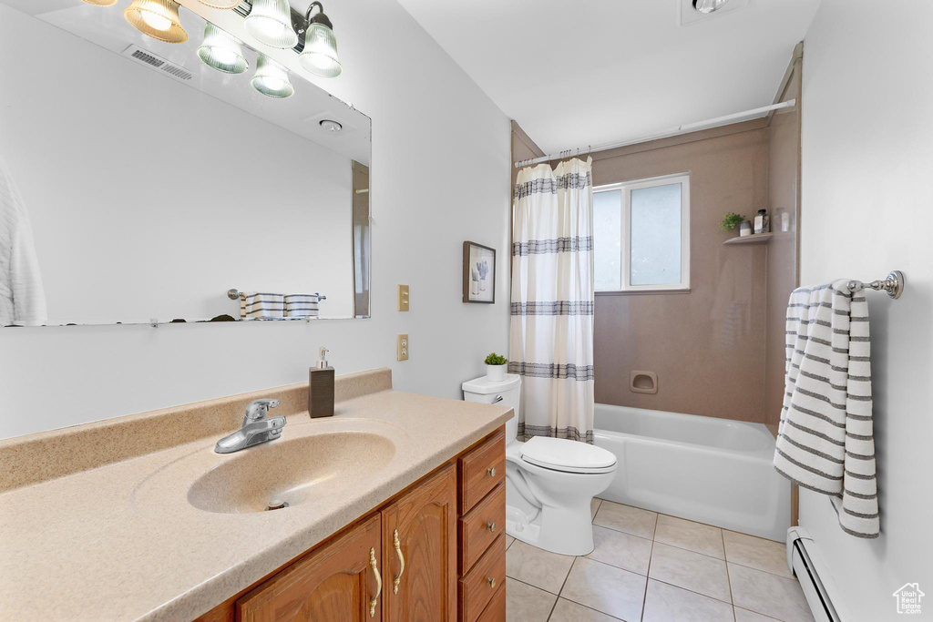 Bathroom featuring baseboard heating, toilet, tile patterned floors, vanity, and shower / bathtub combination with curtain