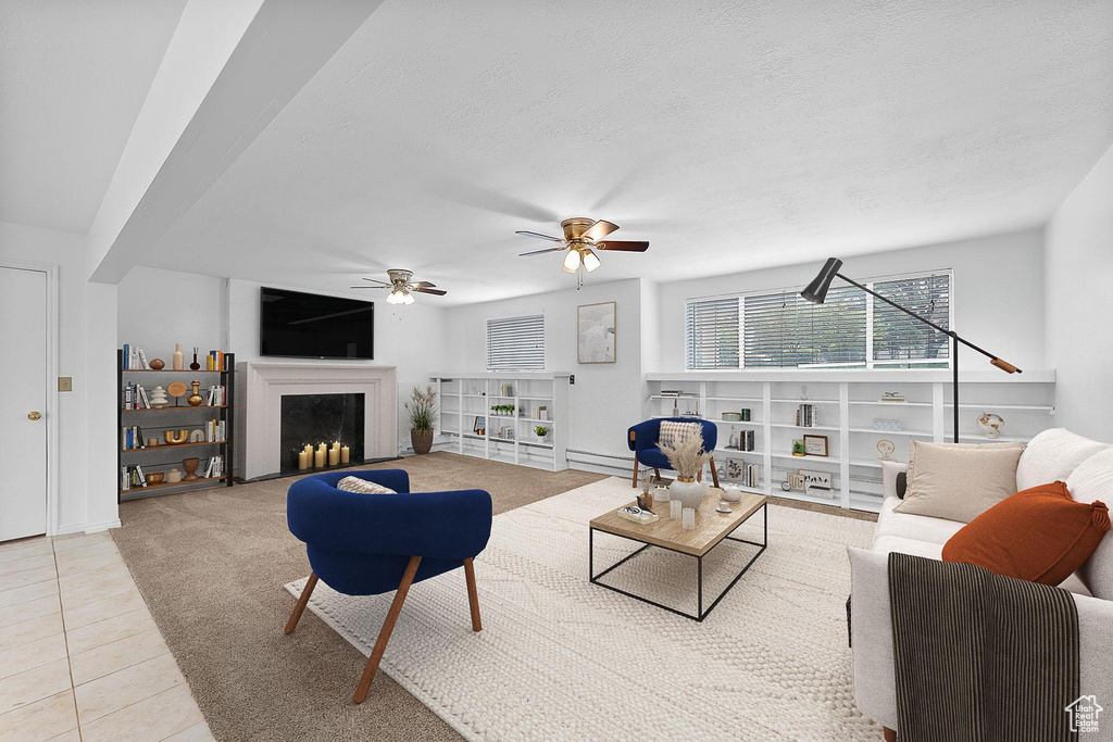 Tiled living area with a fireplace, ceiling fan, baseboards, and a textured ceiling