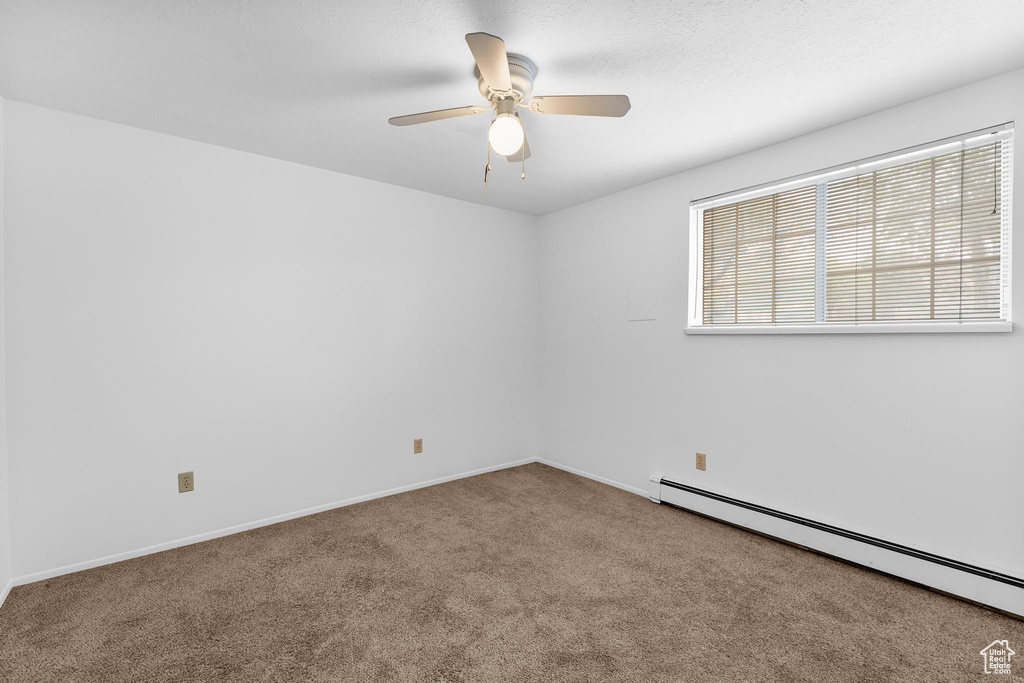 Spare room with a baseboard heating unit, carpet flooring, ceiling fan, and baseboards