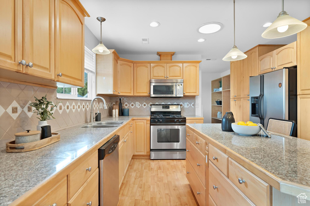 Kitchen featuring appliances with stainless steel finishes, a sink, light brown cabinetry, light wood-style floors, and tasteful backsplash
