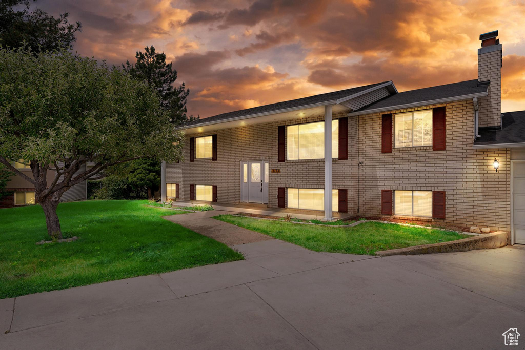 Bi-level home featuring brick siding, a chimney, a lawn, concrete driveway, and a garage