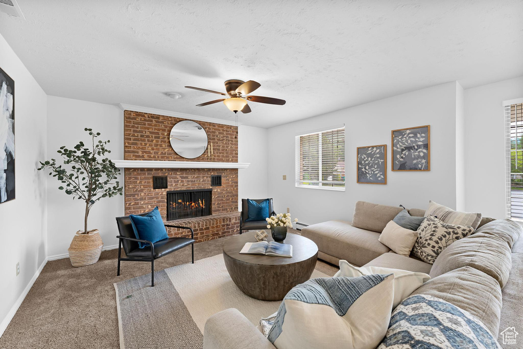 Carpeted living area with ceiling fan, a fireplace, baseboards, and a textured ceiling