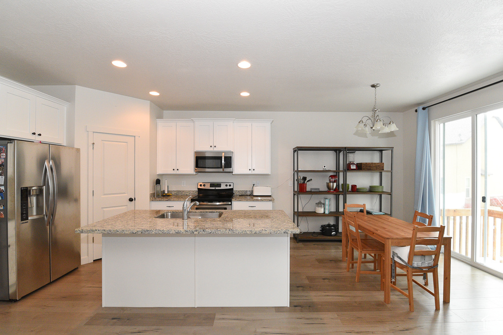 Kitchen featuring appliances with stainless steel finishes, a chandelier, a sink, light wood-style flooring, and white cabinets