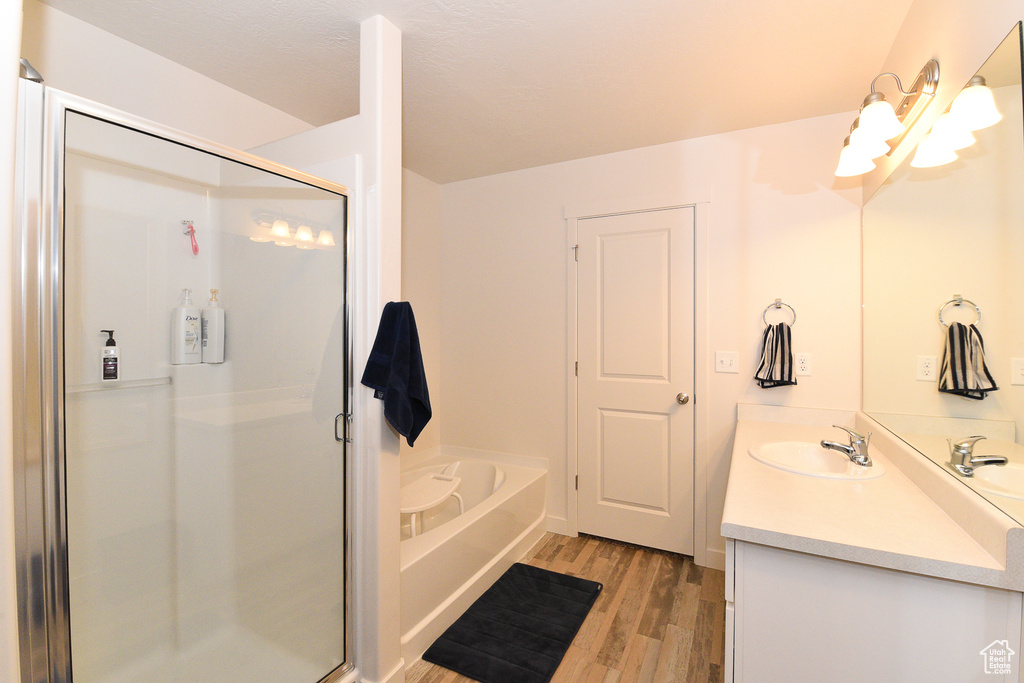Bathroom featuring wood finished floors, a stall shower, vanity, and a bath