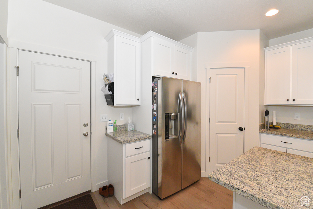 Kitchen featuring stainless steel fridge with ice dispenser, light wood-type flooring, white cabinets, light stone counters, and recessed lighting