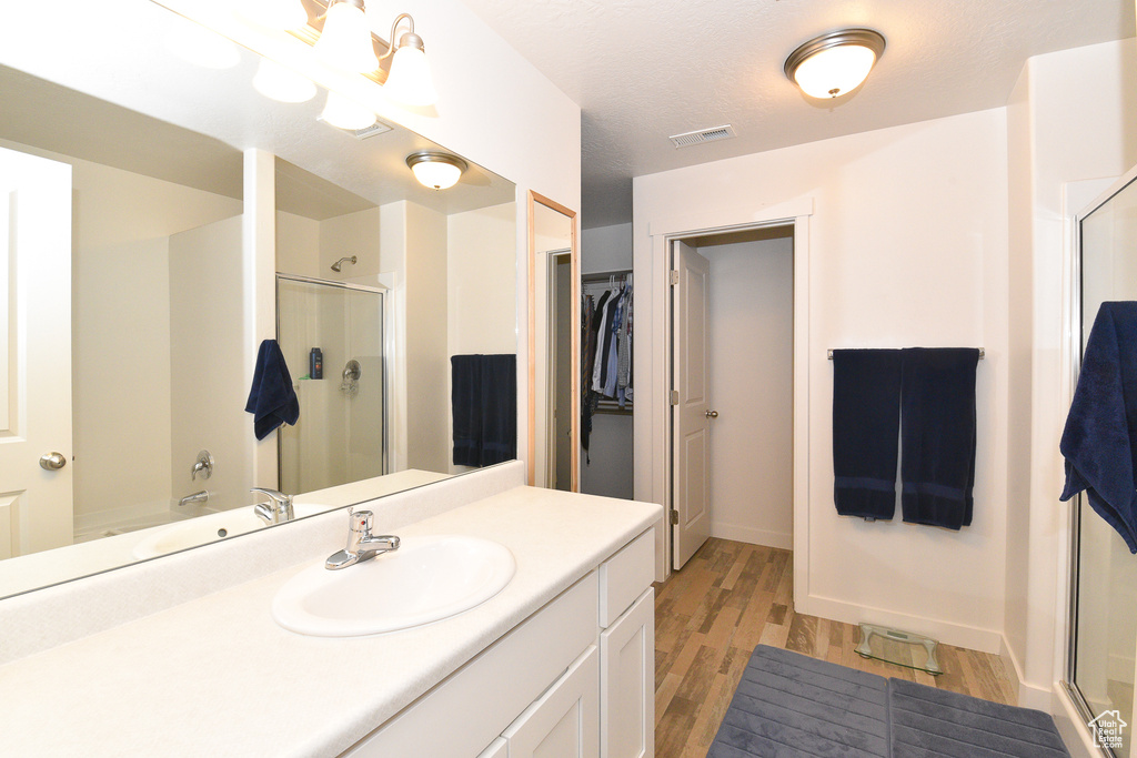 Bathroom featuring a stall shower, wood finished floors, baseboards, vanity, and a walk in closet