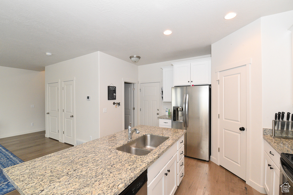 Kitchen featuring stainless steel refrigerator with ice dispenser, a sink, light wood finished floors, white cabinets, and recessed lighting