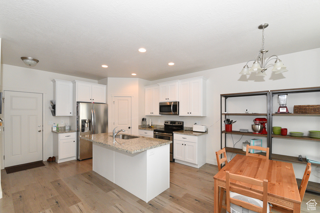 Kitchen with appliances with stainless steel finishes, a sink, light wood-style flooring, white cabinets, and recessed lighting