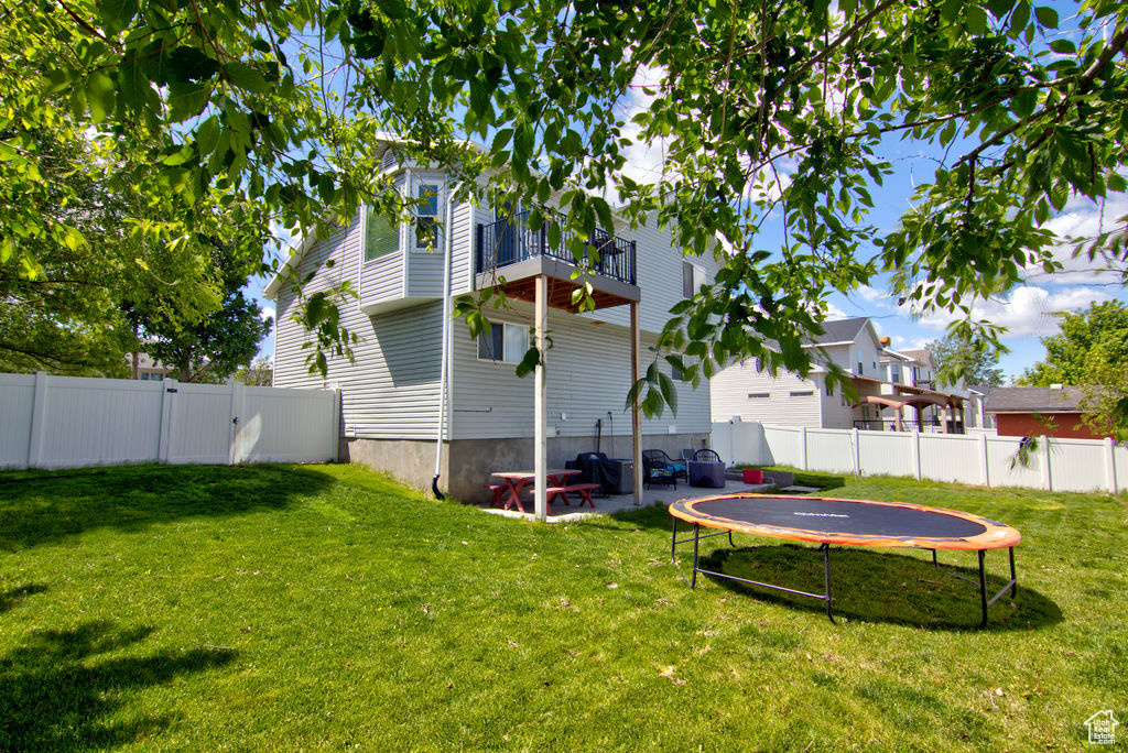 View of yard with a trampoline, a balcony, a patio, and a gate