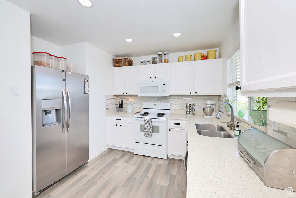 Kitchen featuring white appliances, a sink, light wood-style floors, tasteful backsplash, and white cabinetry
