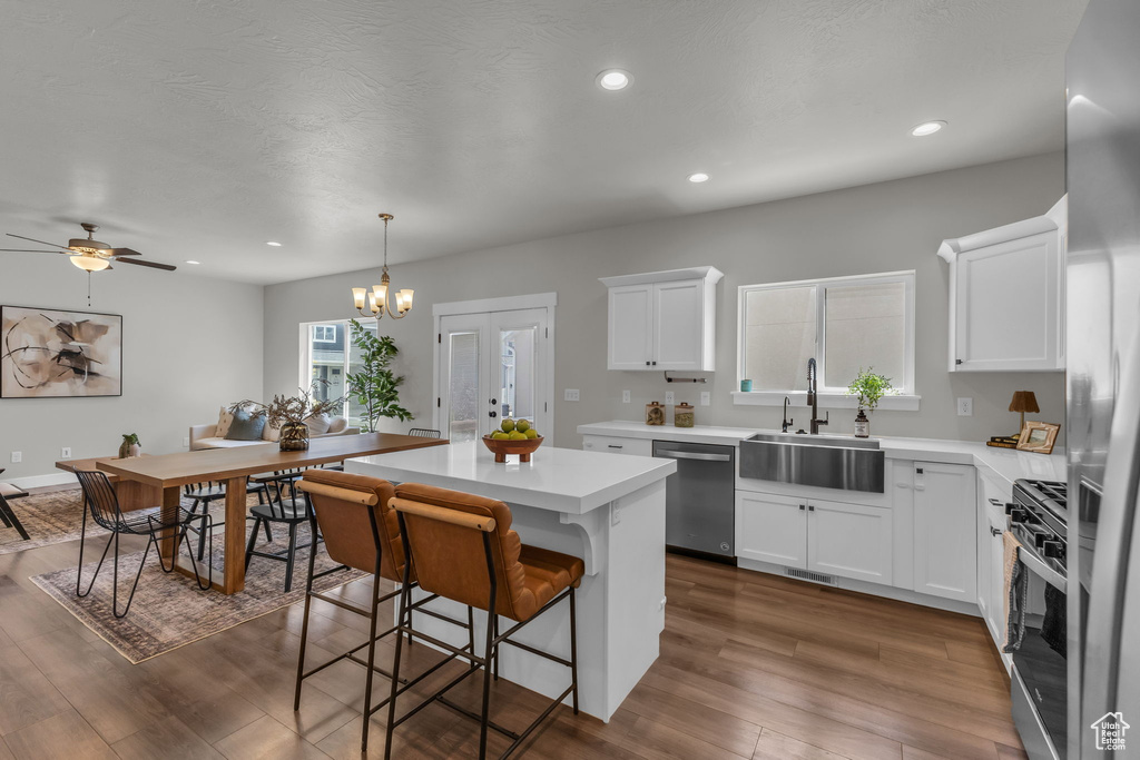 Kitchen featuring appliances with stainless steel finishes, a sink, a kitchen island, light countertops, and a kitchen breakfast bar