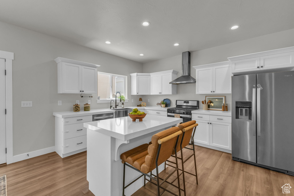Kitchen with appliances with stainless steel finishes, wall chimney exhaust hood, light countertops, light wood-style flooring, and recessed lighting