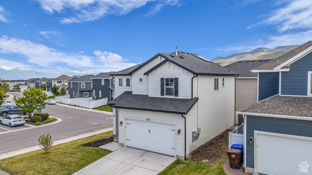 View of side of property with roof with shingles, an attached garage, driveway, a residential view, and a mountain view